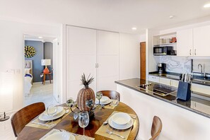 A dining area with a round table set for four, a kitchen with white cabinets and a microwave, and a hallway leading to a bedroom. - Cerro Colorado Condo | Condo in Cabo San Lucas (Cabo San Lucas)