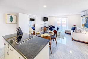 A modern kitchen with a central island, dining area with chairs, a sofa, and a TV mounted on the wall. - Cerro Colorado Condo | Condo in Cabo San Lucas (Cabo San Lucas)
