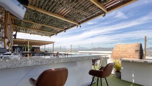 A rooftop bar with a stone counter, two bar stools, a grill, and a view of the cityscape. - Dog-friendly hotel suite with ocean-view rooftop infinity pool, central AC & gym (Cabo San Lucas)