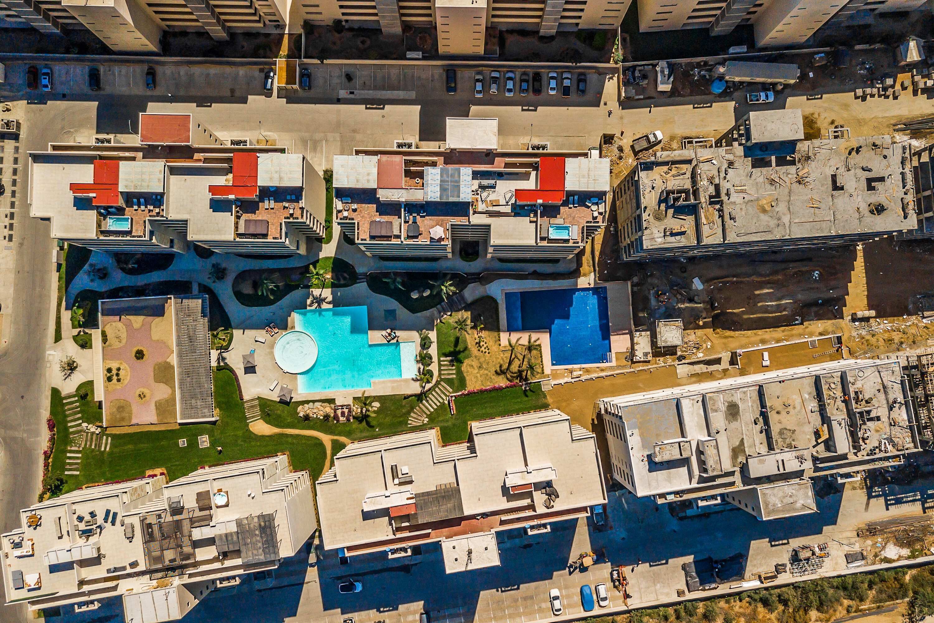 Luftaufnahme eines Wohnkomplexes mit mehreren Gebäuden, einem zentralen Schwimmbad und umgebender Bepflanzung.