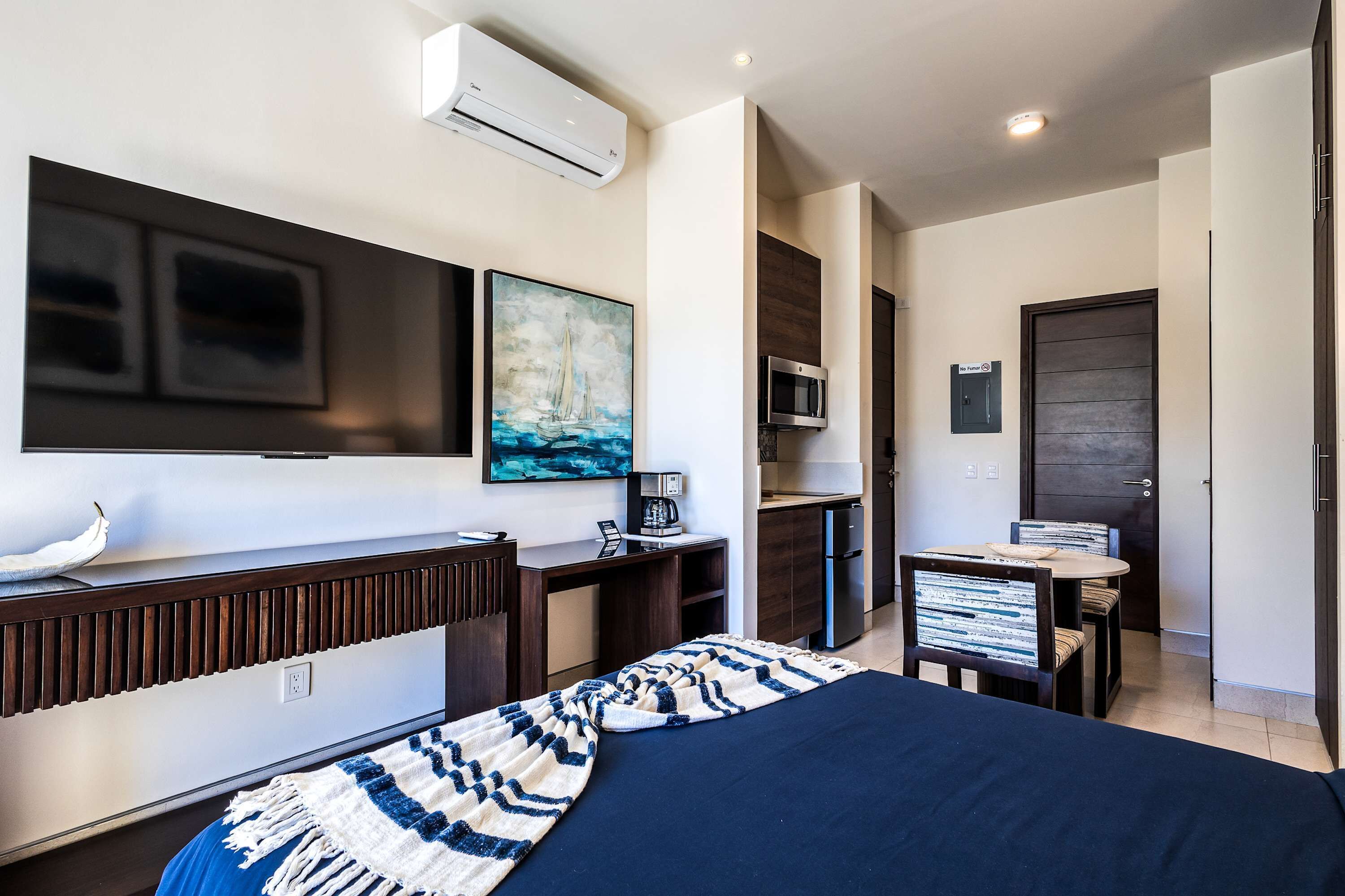 A modern hotel room with a bed, desk, chair, TV, microwave, and a door.