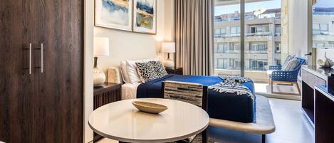 Habitación de hotel moderna con cama, sofá, mesa redonda y ventana grande con vistas a edificios.