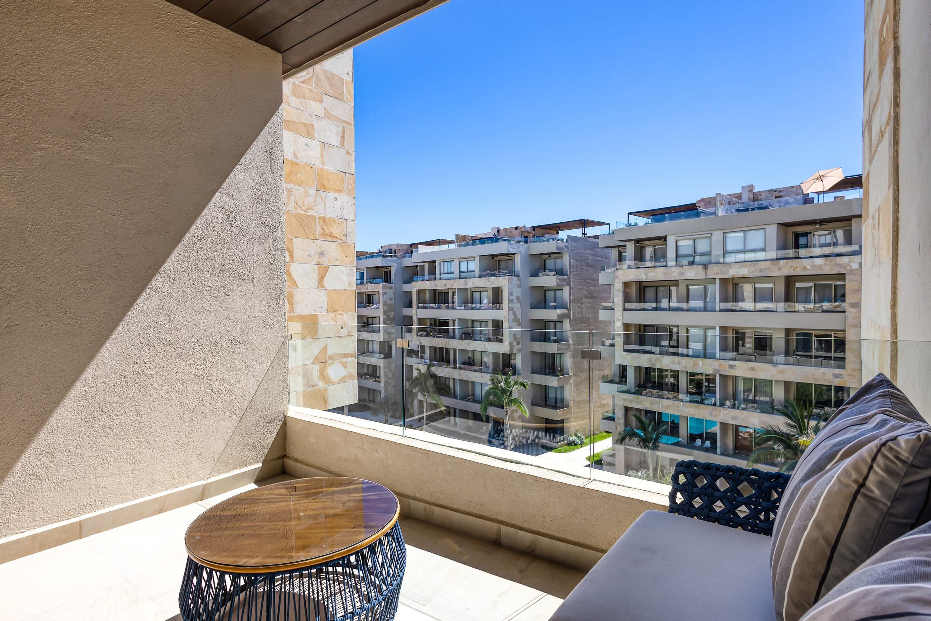 Un balcon donnant sur un immeuble à plusieurs étages, une table ronde en bois et un canapé avec des coussins.