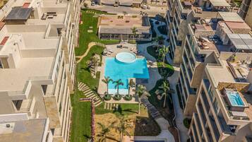 A high-rise hotel with multiple balconies, a central swimming pool, and surrounding greenery.