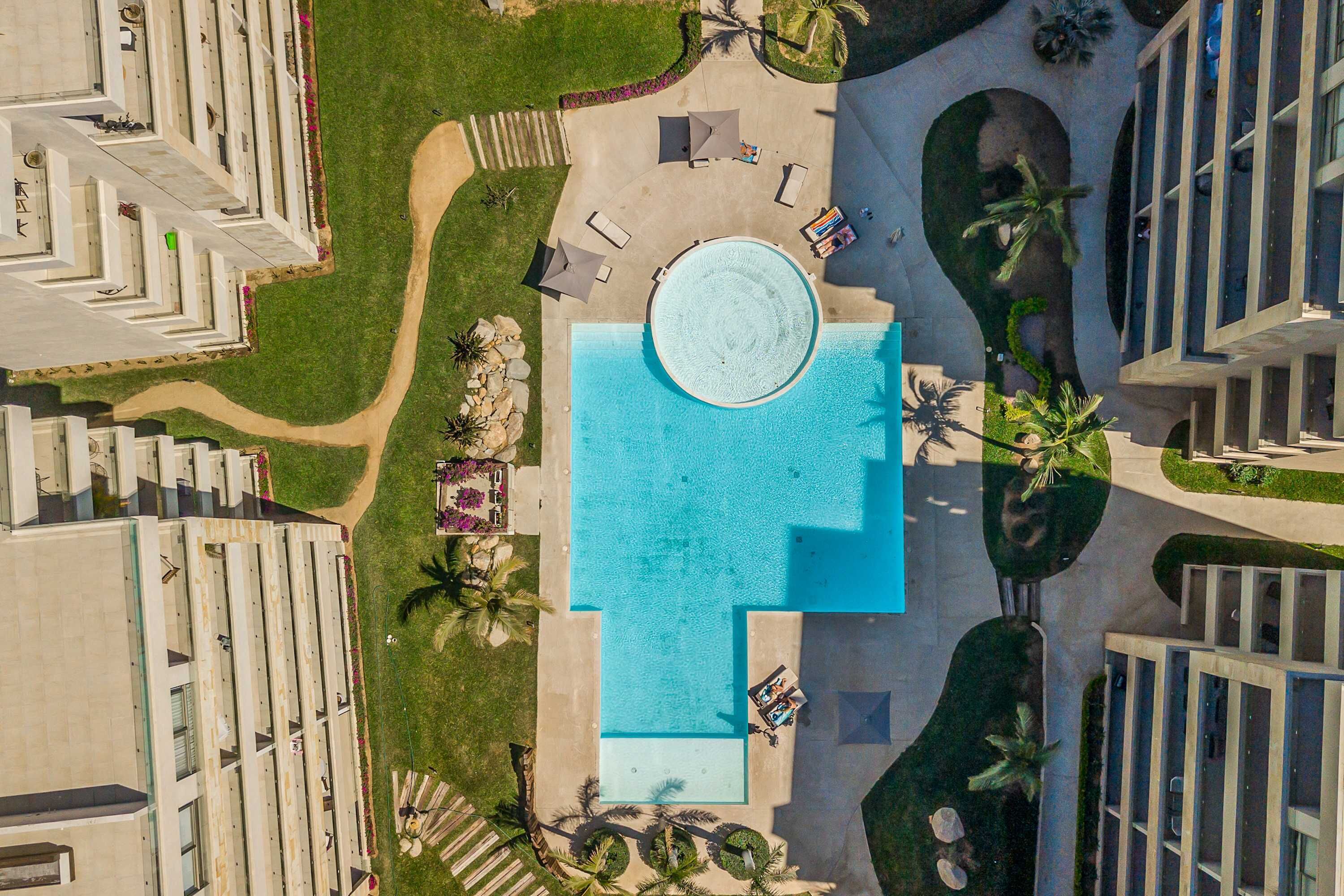 Eine Luftaufnahme eines Resorts mit einem zentralen Pool, mehreren Gästezimmern und einer gepflegten Rasenfläche.