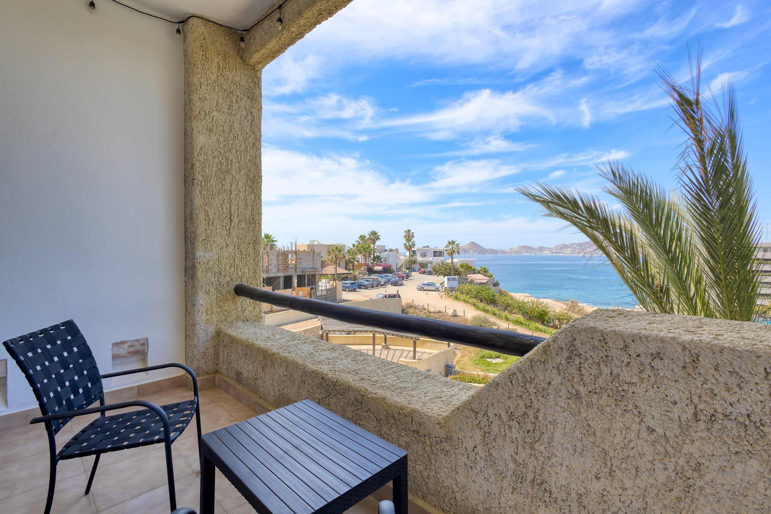 A balcony with a view of the sea, a chair, and a table.