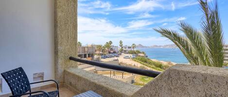 A balcony with a view of the sea, a chair, and a table.