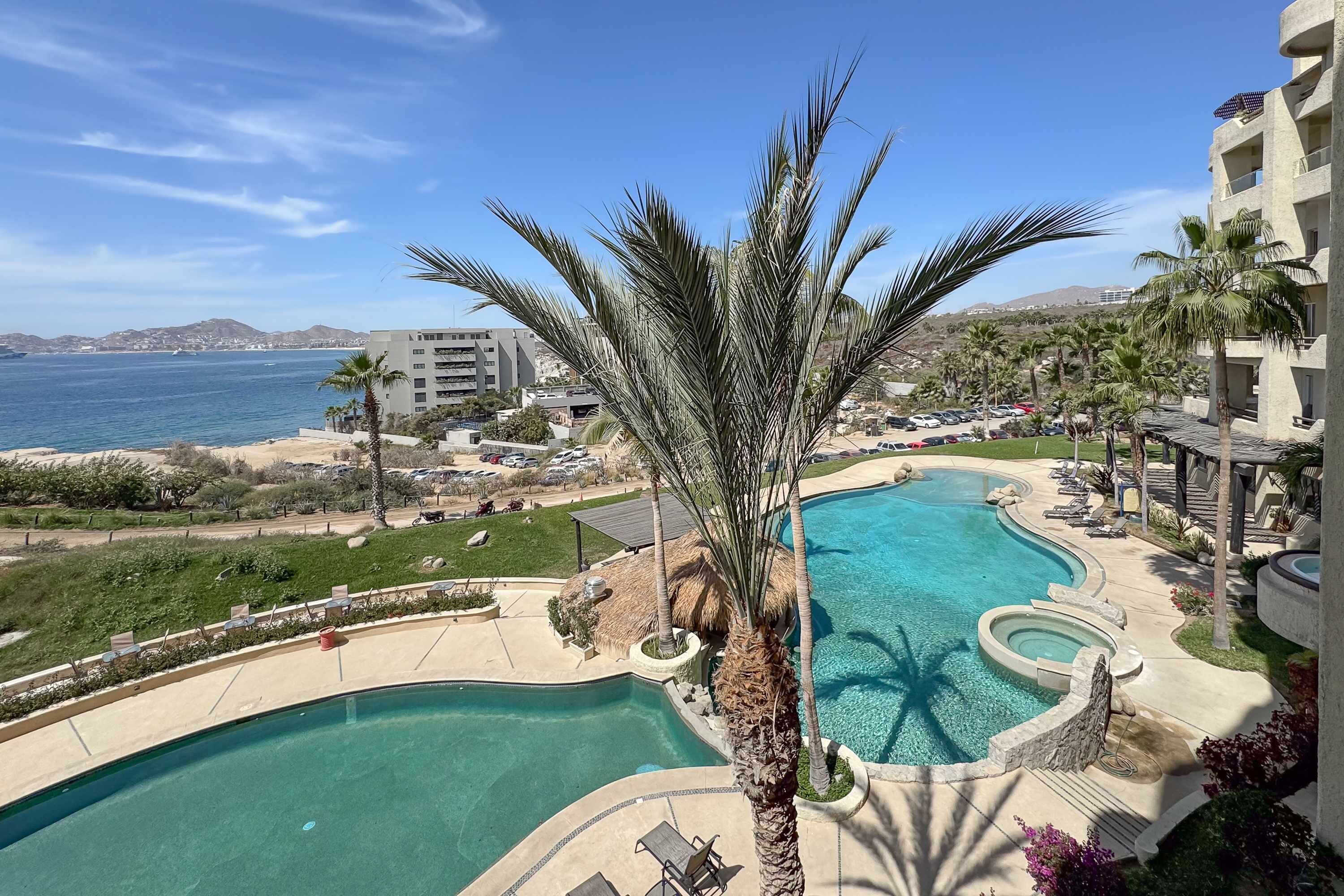 Un complexe hôtelier doté d’une piscine, de palmiers et offrant une vue sur la mer.