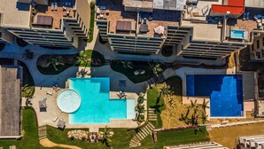 Vista aérea de un hotel con varias piscinas, zonas de estar al aire libre y una piscina circular central.