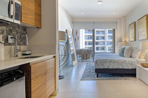 Ein modernes Hotelzimmer mit Küchenzeile, einem großen Bett und Blick auf die Stadt.
