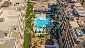 Un hotel moderno de altura con varios balcones, una piscina central y abundante vegetación alrededor.