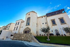 A large building with a stone entrance, multiple windows, and a green lawn area. - Stylish condo w/pool, ocean views, fitness & patio (Cabo San Lucas)