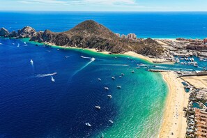 An aerial view of a coastal area with a beach, boats, and buildings. - Luxury Cabo condo with multiple pools, pickleball, gym & rooftop (Cabo San Lucas)