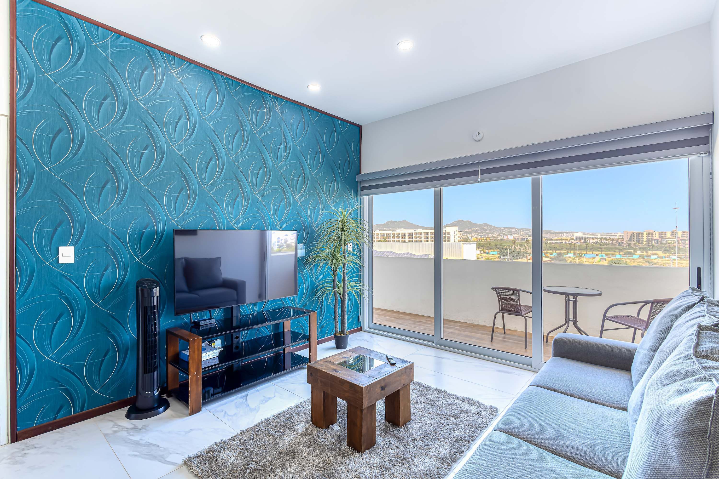 A living room with a TV, a coffee table, a sofa, and a balcony with a view.