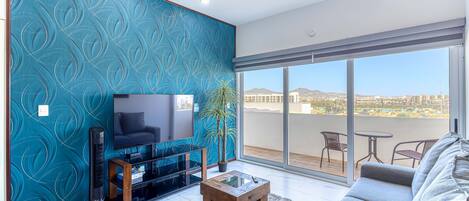 A living room with a TV, a coffee table, a sofa, and a balcony with a view.
