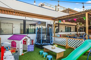 Ein Kinderspielbereich mit einem kleinen Haus, einem Trampolin und einer Rutsche.