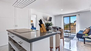 A modern kitchen with a central island, a dining area with a table and chairs, and a living room with a sofa and a TV. - Morgan Residences 508A @ Boutique Hotel with pool, gym, spa (Cabo San Lucas)
