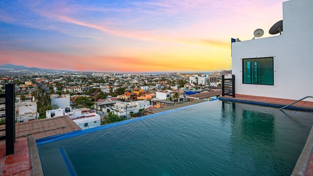 An infinity pool with a city view, a white building with satellite dishes, and a clear sky. - Morgan Residences 508A @ Boutique Hotel with pool, gym, spa (Cabo San Lucas)