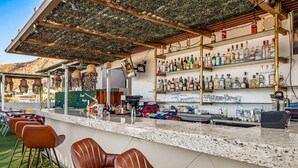 A bar area with a counter, bar stools, and shelves of liquor bottles. - Morgan Residences 508A @ Boutique Hotel with pool, gym, spa (Cabo San Lucas)