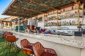 Una zona de bar con mostrador, taburetes, estantes llenos de botellas y vistas a un paisaje montañoso.