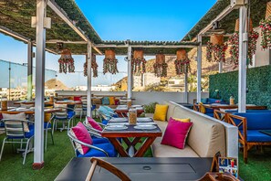 Un espacio al aire libre con mesas, sillas, un sofá y decoraciones colgantes.