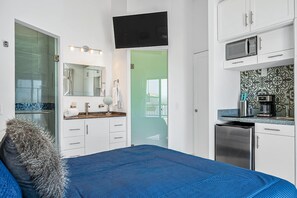 Un dormitorio con cama, un baño con ducha, una cocina con microondas y un televisor montado en la pared.