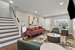 A living room with a staircase, a sofa, a coffee table, and a television.