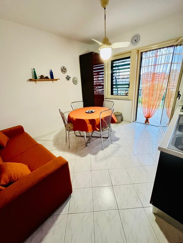 Un comedor con una mesa redonda, sillas, ventilador de techo y una barra de cocina.
