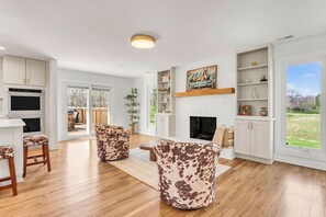 Ein großzügiges Wohnzimmer mit Kamin, Holzboden und einem großen Fenster mit Blick ins Freie.