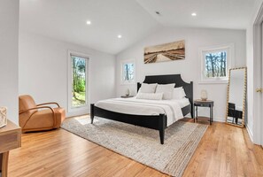 Ein Schlafzimmer mit einem Bett, einem Sessel, einem Nachttisch, einem Spiegel und einem Fenster.