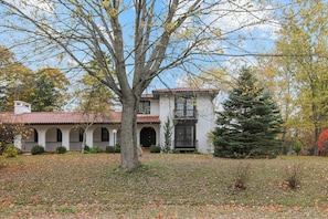 A two-story building with a red-tiled roof, a large tree in front, and a well-maintained lawn.