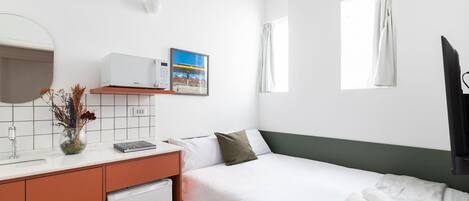 A hotel room with a bed, a small desk with a microwave, a sink, a mirror, and a window with curtains.