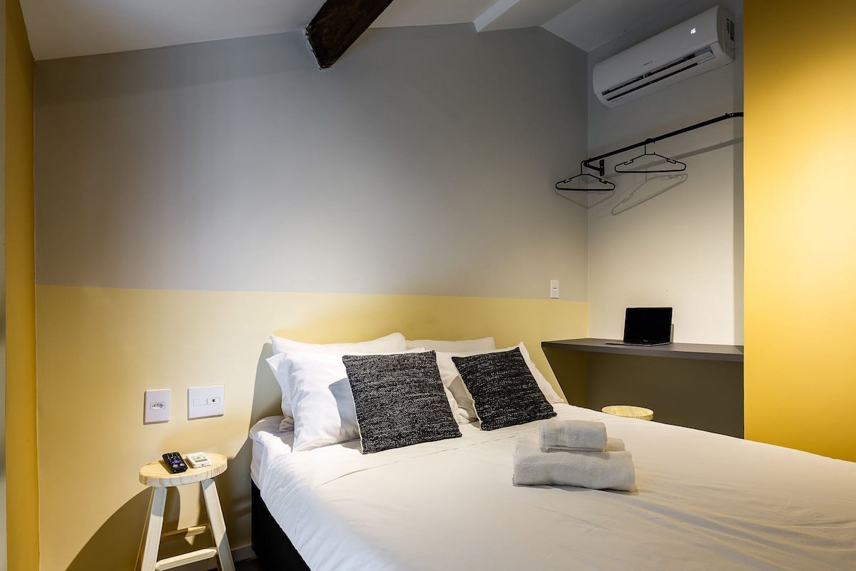 Habitación de hotel con cama, mesita de noche y aire acondicionado de pared.