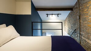 A bedroom with a bed, a headboard, a brick wall, and a ceiling with exposed beams. - ZEST Pedroso (São Paulo)