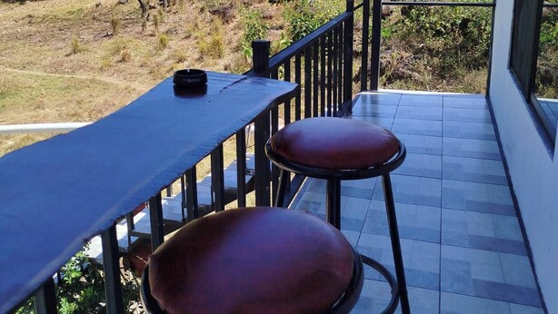 A covered outdoor seating area with a table and two stools, overlooking a natural landscape. - Serene Cabin Retreat in Cuajiniquil, Costa Rica (La Cruz)