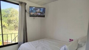 A bedroom with a bed, a TV mounted on the wall, and a window with curtains. - Serene Cabin Retreat in Cuajiniquil, Costa Rica (La Cruz)