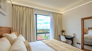Quarto de hotel com uma cama grande, uma escrivaninha, uma cadeira e vista para o horizonte urbano pela janela.