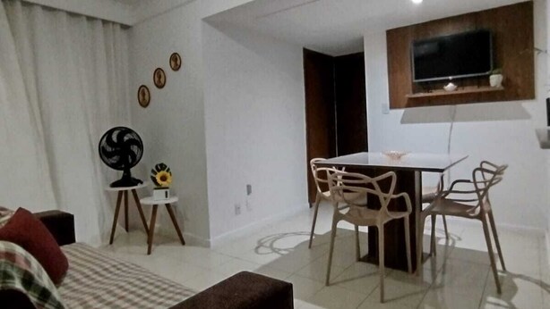 Una sala de estar moderna con un sofá, una mesa de comedor con sillas, un televisor montado en la pared y un ventilador de techo.