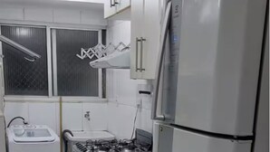 Una cocina con gabinetes blancos, un refrigerador de acero inoxidable, una estufa a gas y un ventanal con persianas.