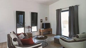 A modern living room with a sofa, armchair, coffee table, TV stand, and large windows with curtains. - 3-bedroom house, located 2mns from the Nantes-Brest canal and its walks! (Plessé)