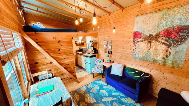 A cozy cabin interior with a dining area, a sofa, a kitchen, and a large butterfly mural. - Bamboo bungalow at Camp David. Pond-front, pet friendly tiny home retreat (Saluda)