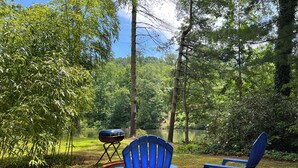 A campsite with two blue chairs, a portable grill, and a small brick structure. - Bamboo bungalow at Camp David. Pond-front, pet friendly tiny home retreat (Saluda)