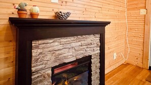 A fireplace with a stone facade, a mounted television, and a wooden wall with horizontal planks. - Bamboo bungalow at Camp David. Pond-front, pet friendly tiny home retreat (Saluda)
