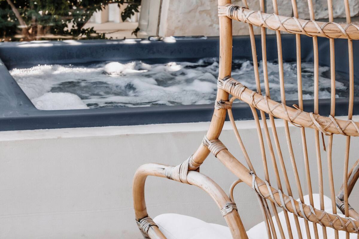 A wicker chair with a cushion, positioned near a stone wall and a water feature.