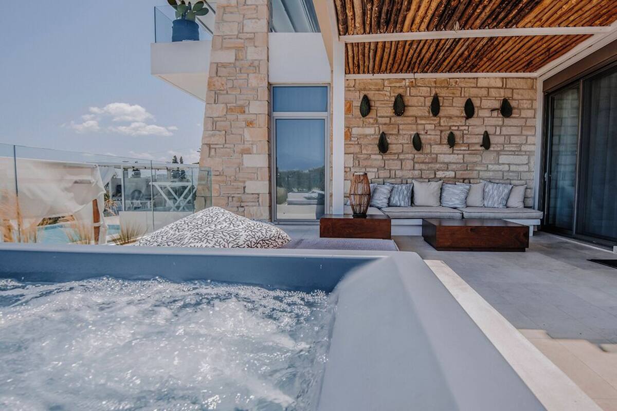 A modern outdoor hot tub area with a stone wall, a wooden ceiling, and a seating area with cushions.