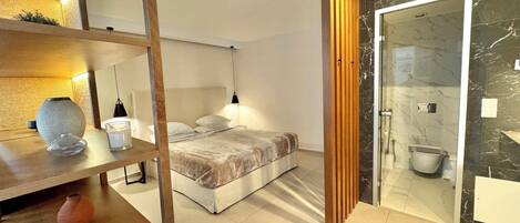 Un dormitorio moderno con cama, mesitas de noche, un jarrón y un baño con cabina de ducha de vidrio.