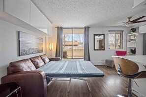 Moderni huone, jossa on avattava vuodesohva, ruokapöytä ja kattotuuletin.