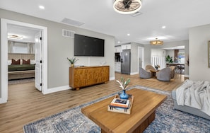 A modern living room with a wooden coffee table, a flat-screen TV mounted on the wall, and a dining area with chairs and a table. - Newly Renovated Spacious 5-bedroom house with Pool and Hot Tub in Largo (Largo)