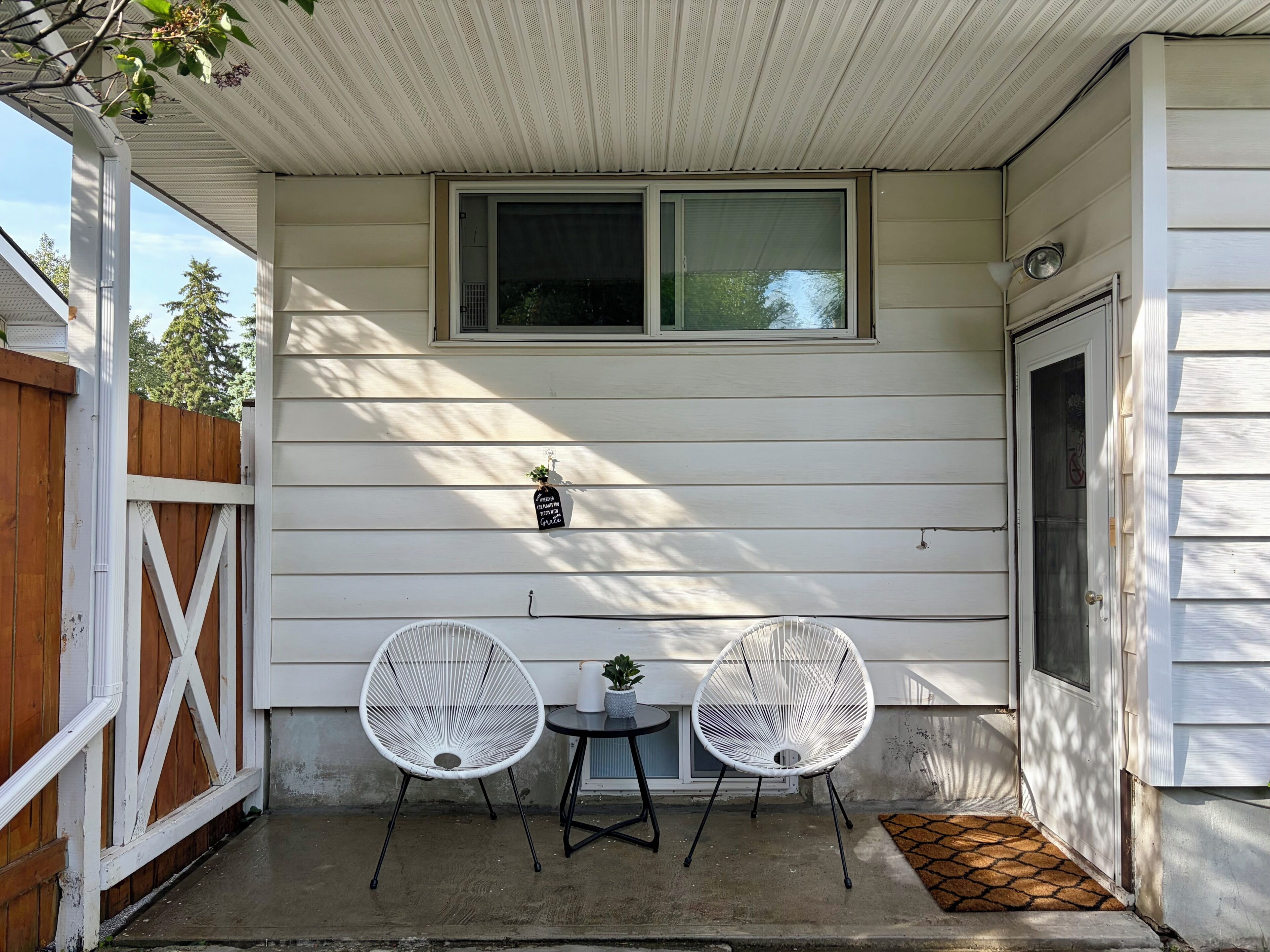 A covered porch with two white chairs, a small table, and a potted plant.