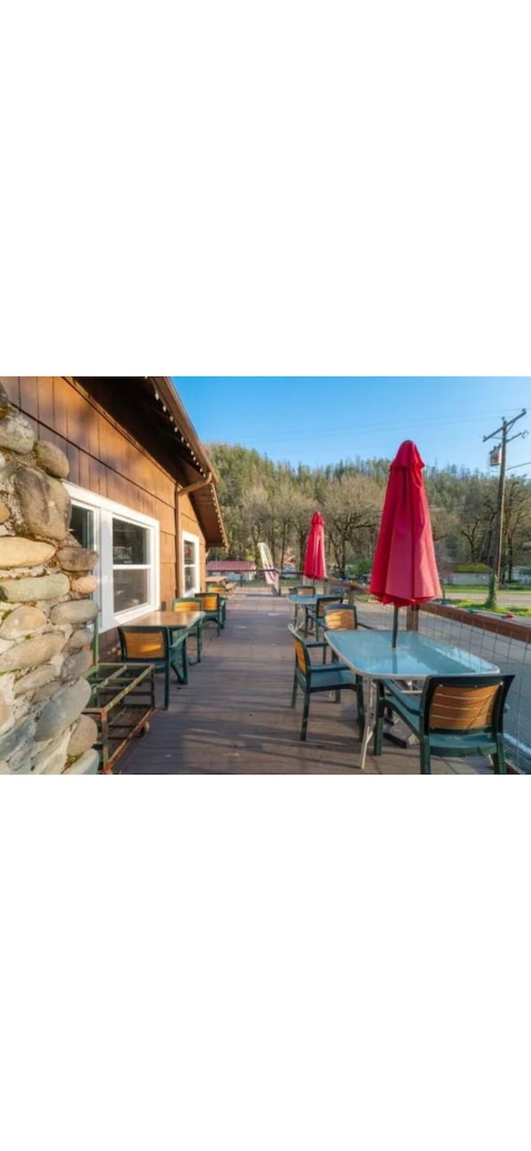 An outdoor patio with stone walls, wooden tables, and red umbrellas.